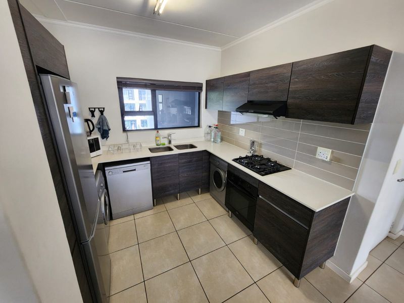Modern kitchen featuring dark wood-grain cabinetry, stone-look countertops, a gas hob, built-in oven, and integrated space for appliances with neutral tiled flooring.