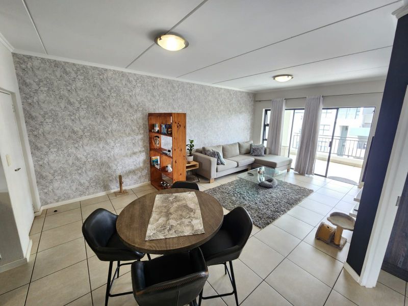 Spacious open-plan living and dining area featuring tiled flooring, a textured feature wall, and large sliding doors leading to a private balcony.