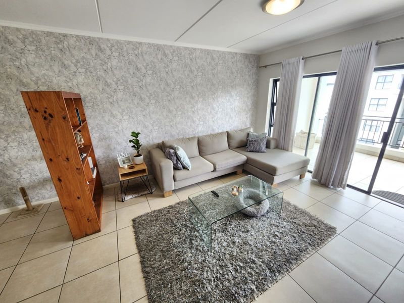 A bright living room featuring tiled flooring, a textured feature wall, and large sliding glass doors providing access to the balcony.