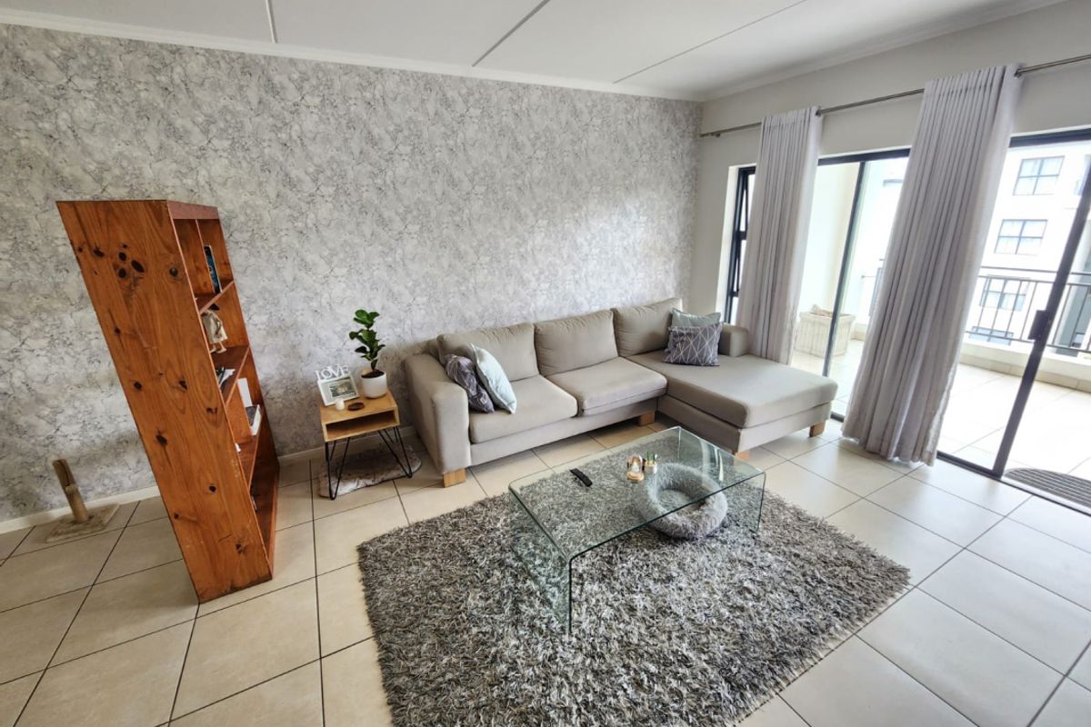 A bright living room featuring tiled flooring, a textured feature wall, and large sliding glass doors providing access to the balcony.