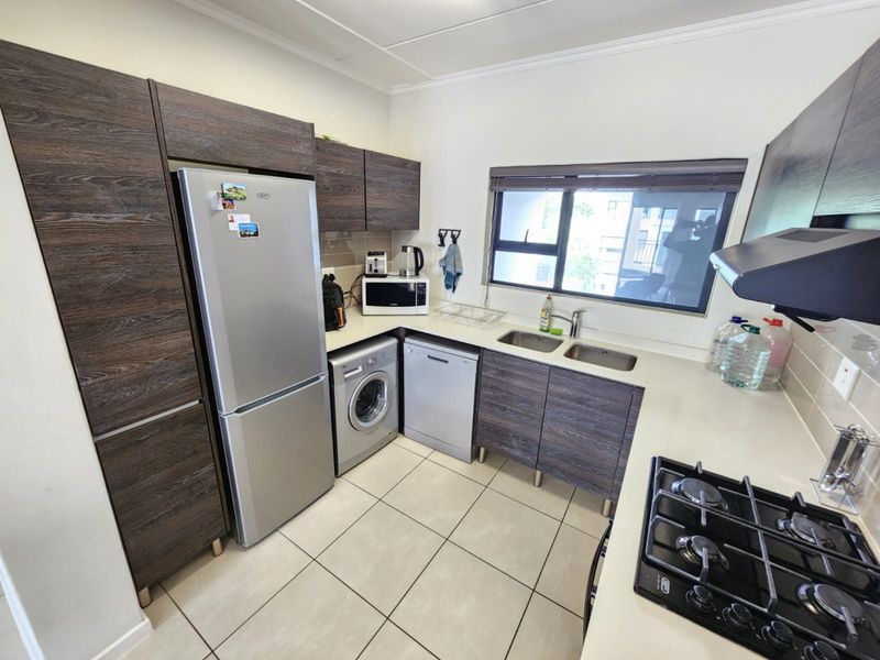 A functional kitchen featuring dark wood-grain cabinetry, stone countertops, a gas hob with extractor, and integrated space for laundry and dishwashing appliances.