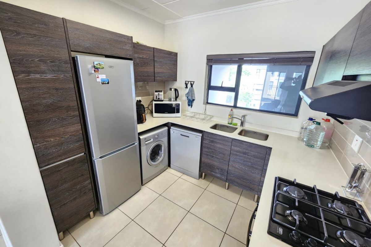 A functional kitchen featuring dark wood-grain cabinetry, stone countertops, a gas hob with extractor, and integrated space for laundry and dishwashing appliances.