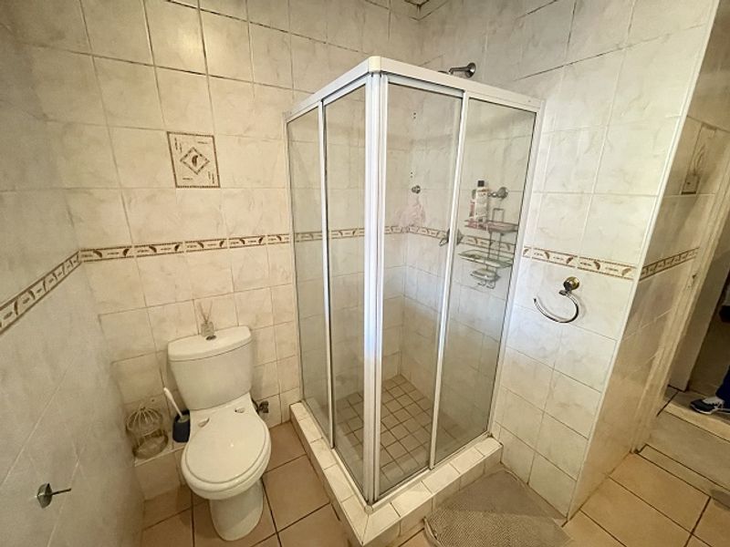 A functional bathroom featuring a corner shower enclosure, toilet, and neutral wall and floor tiling.