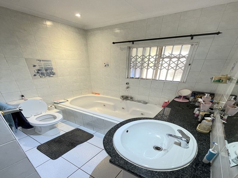A functional bathroom featuring a built-in bathtub, granite-topped vanity with a drop-in sink, and tiled finishes throughout.