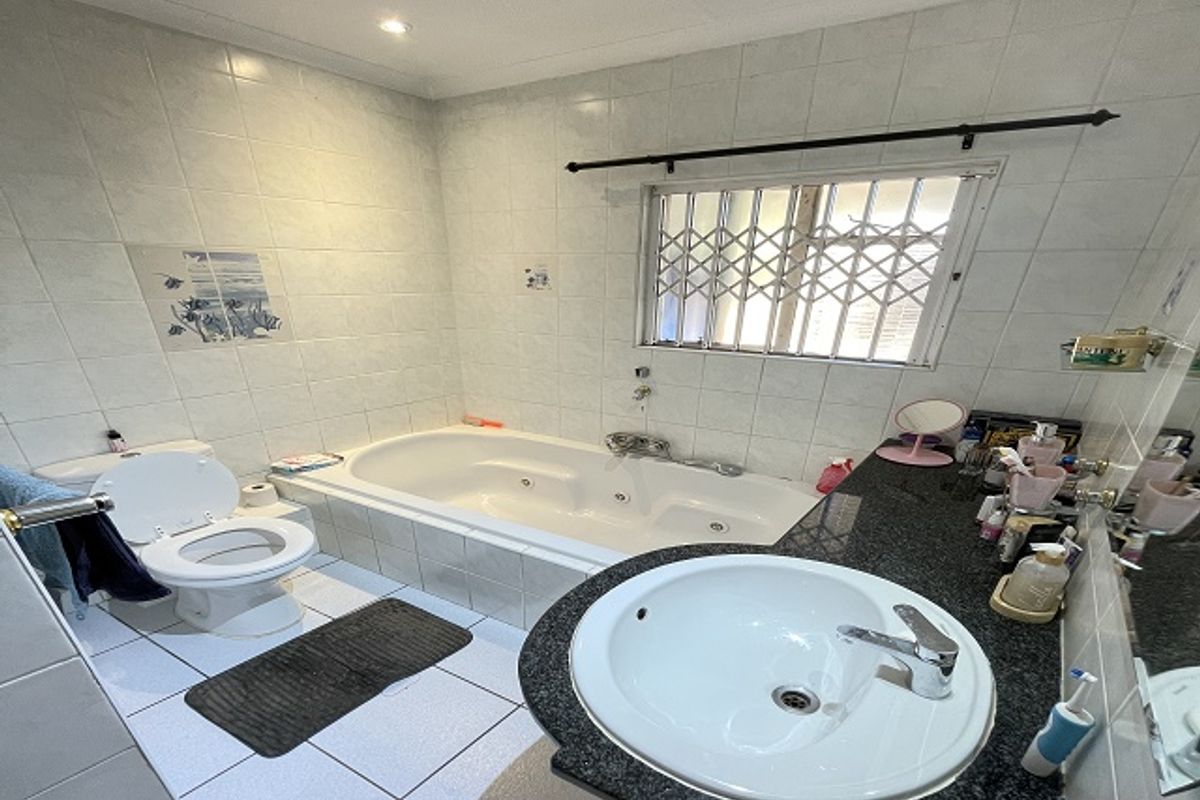 A functional bathroom featuring a built-in bathtub, granite-topped vanity with a drop-in sink, and tiled finishes throughout.
