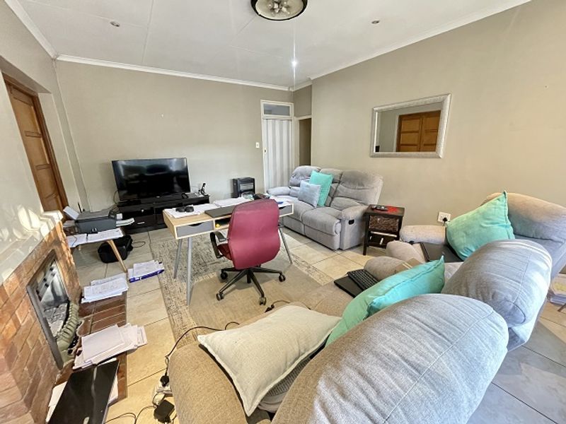 A living room featuring tiled flooring, a brick fireplace, and recessed ceiling lighting, currently utilized as a multi-purpose living and workspace area.