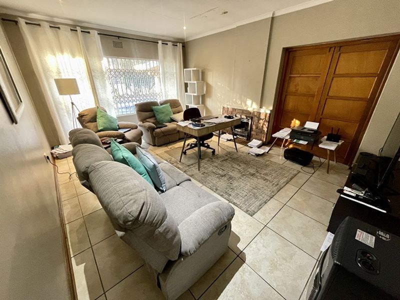 A living room featuring tiled flooring, a brick fireplace, and wooden double doors, offering a functional space with potential for cosmetic updates.