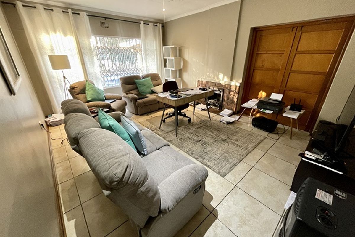A living room featuring tiled flooring, a brick fireplace, and wooden double doors, offering a functional space with potential for cosmetic updates.