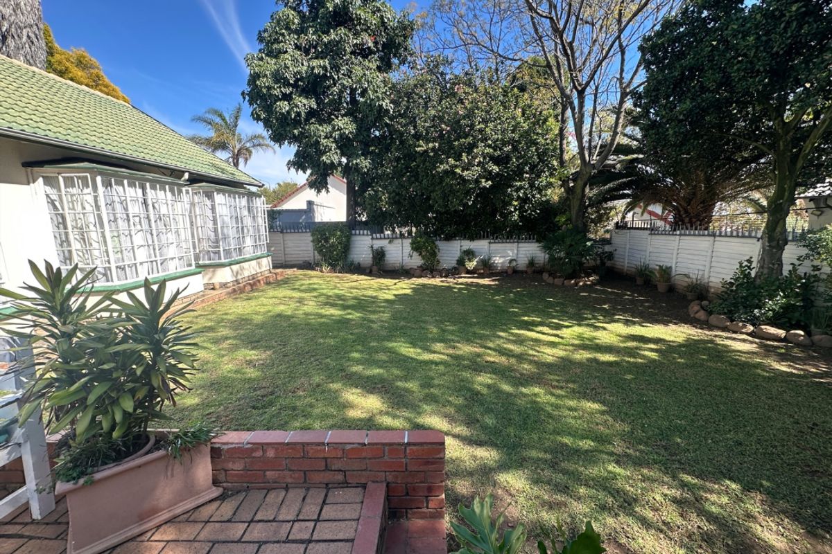 A well-maintained rear garden featuring a brick-paved patio area, a lush lawn, and established perimeter walling.