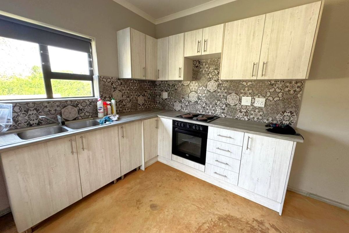 A functional kitchen featuring light wood-grain cabinetry, patterned tile backsplash, built-in oven and hob, and a stainless steel double sink.