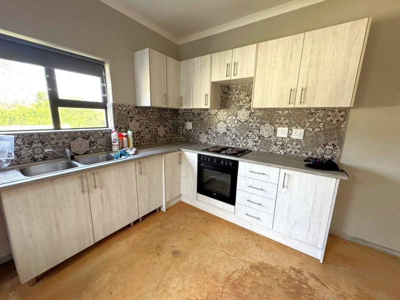 A functional kitchen featuring light wood-grain cabinetry, patterned tile backsplash, built-in oven and hob, and a stainless steel double sink.