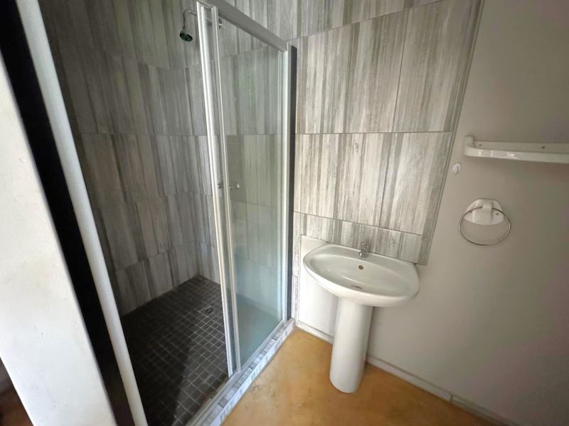 A functional bathroom featuring a glass-enclosed shower, pedestal basin, and neutral wall tiling.