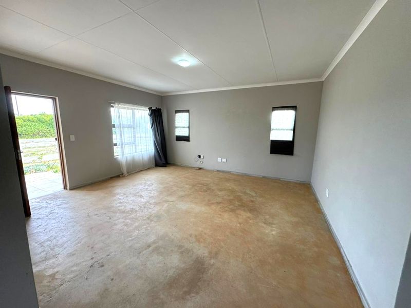An empty, neutrally painted living room featuring tiled flooring, ceiling coving, and direct access to an outdoor area through a side door.