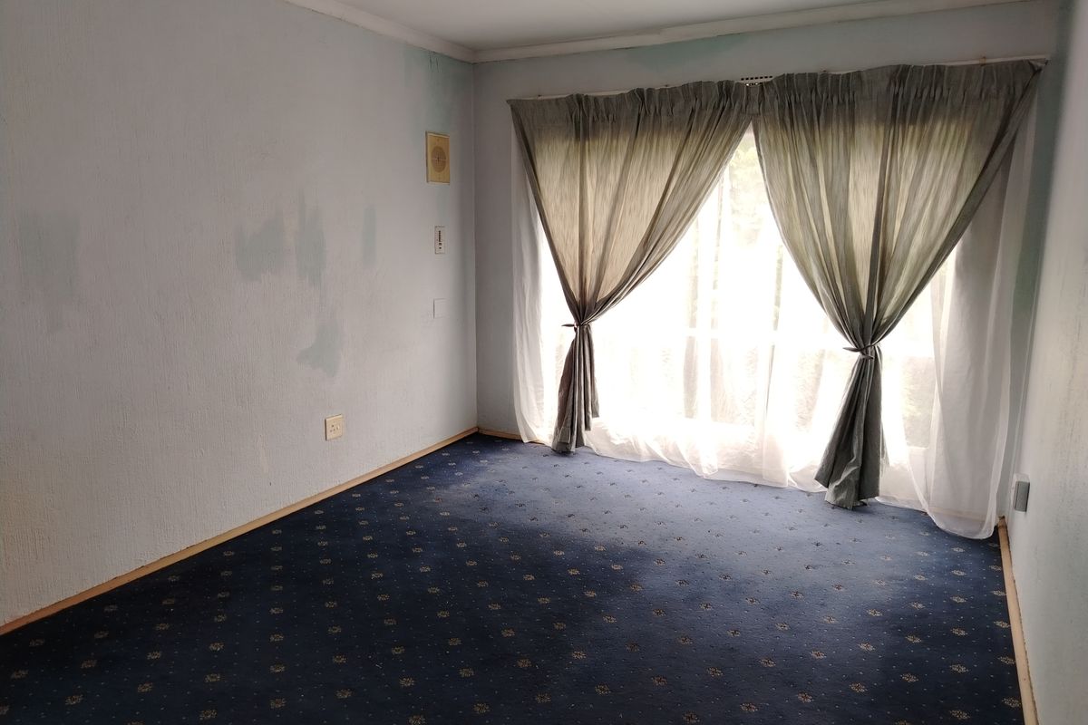 An empty bedroom featuring blue patterned carpeting and a sliding glass door with curtains, requiring cosmetic updates to the walls and flooring.
