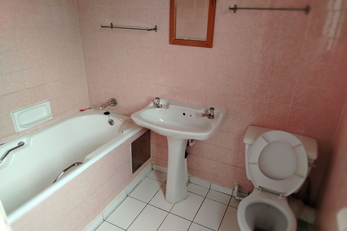 A dated bathroom featuring a pedestal washbasin, bathtub, and toilet with pink wall tiling and white floor tiles.