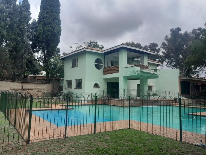 Rear view of a two-story house featuring a swimming pool with safety fencing, a paved surround, and an upper-level balcony.
