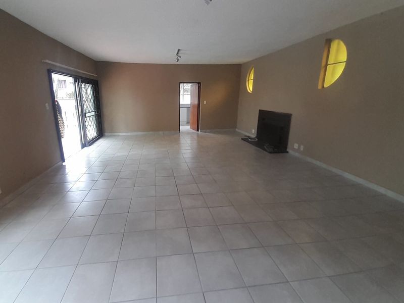 Spacious, empty living room featuring neutral tiled flooring, a built-in fireplace, and sliding glass doors leading to an outdoor area.