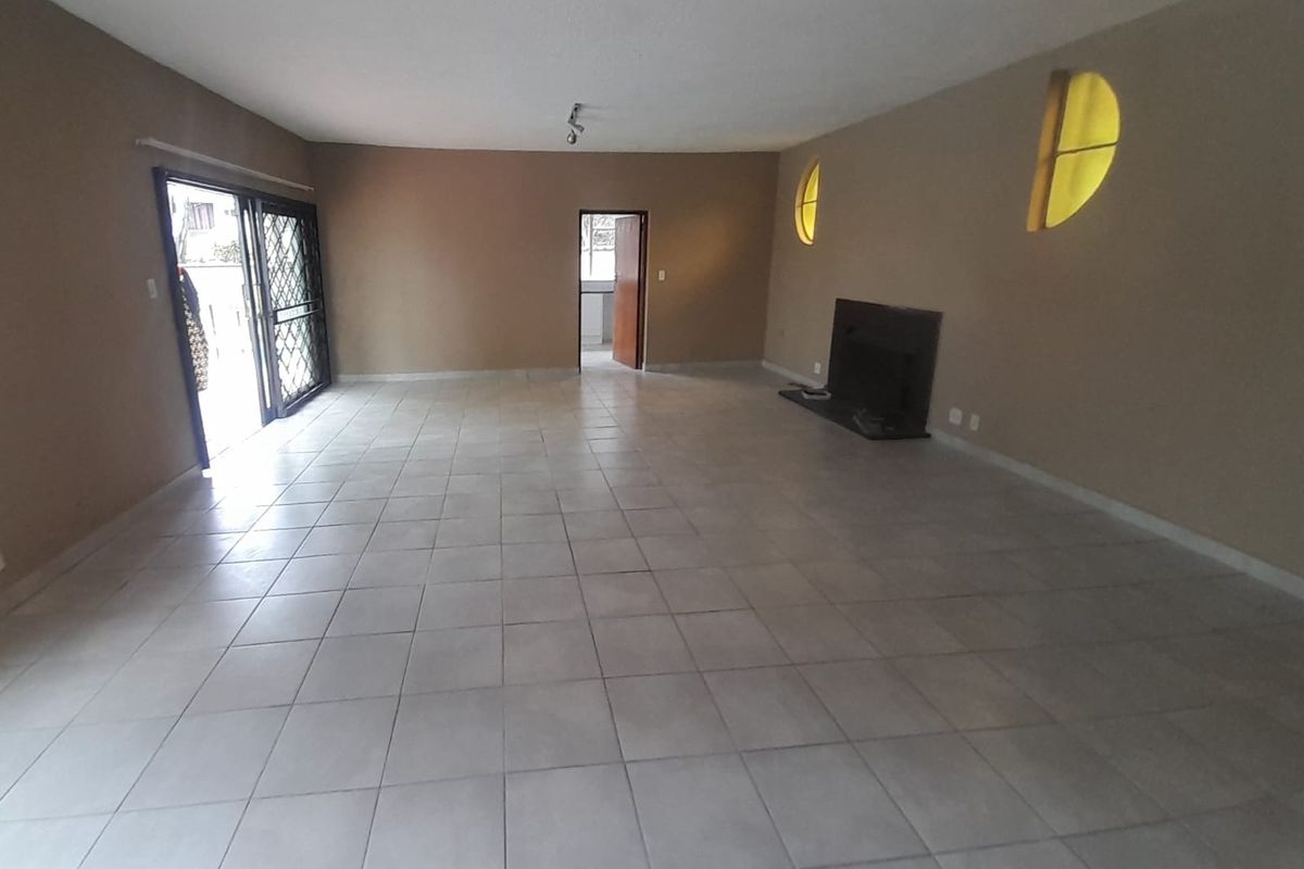 Spacious, empty living room featuring neutral tiled flooring, a built-in fireplace, and sliding glass doors leading to an outdoor area.
