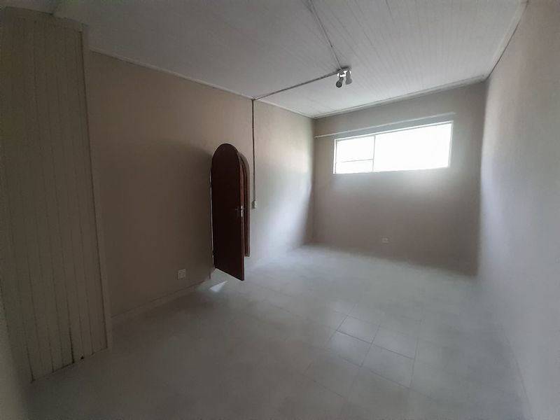An empty bedroom featuring tiled flooring, a built-in cupboard, and an arched door, offering a blank canvas for renovation or interior design.