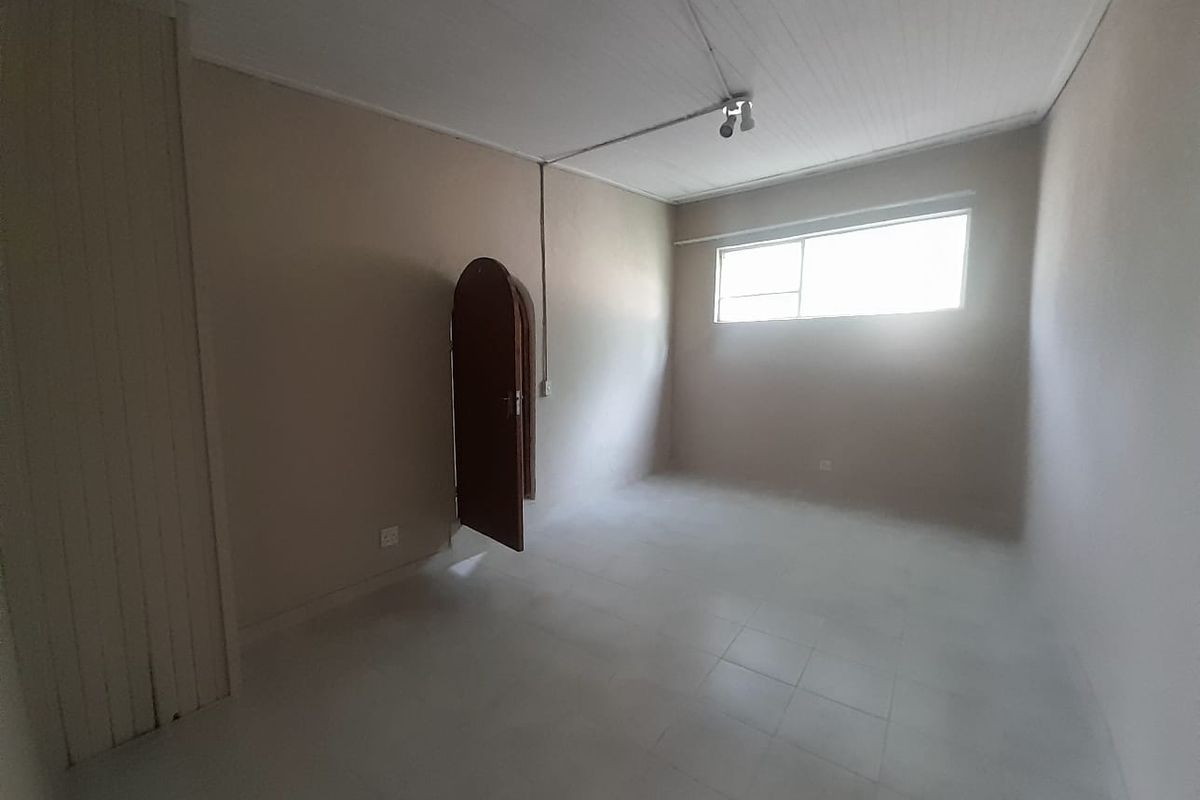 An empty bedroom featuring tiled flooring, a built-in cupboard, and an arched door, offering a blank canvas for renovation or interior design.