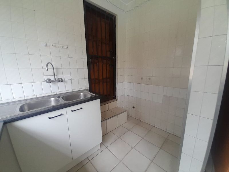 A functional laundry area featuring a double stainless steel sink, tiled splashbacks, and direct access to an exterior door with a security gate.