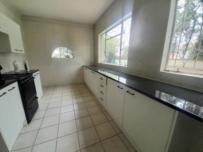 A functional kitchen featuring white cabinetry, dark granite countertops, tiled flooring, and large windows with security bars.