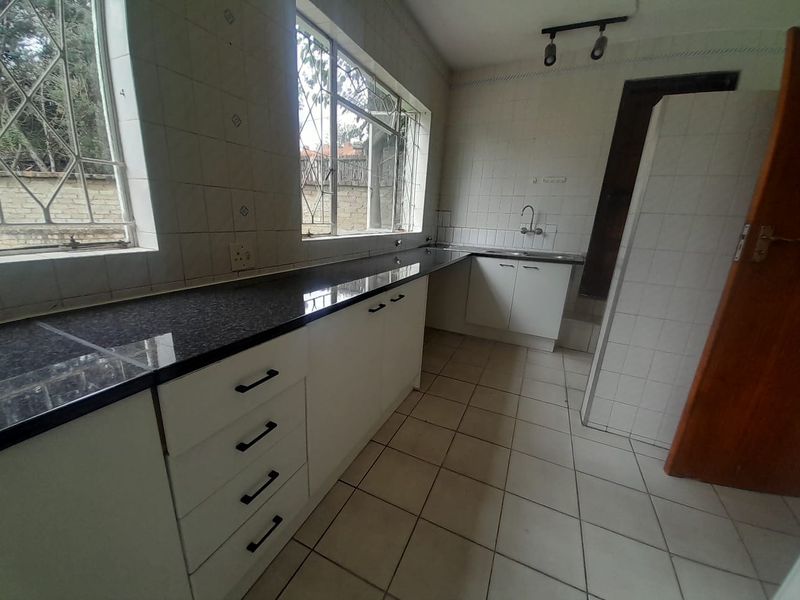 A functional, empty kitchen featuring granite countertops, white cabinetry, tiled walls, and tiled flooring, offering a clean slate for potential updates.