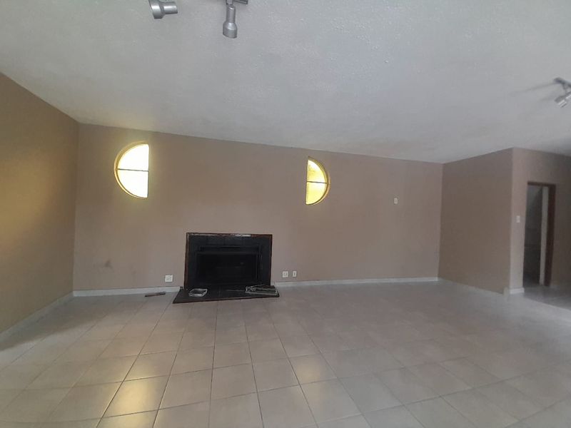 Spacious, empty living room featuring tiled flooring, a built-in fireplace, and distinctive circular windows, offering a blank canvas for renovation.