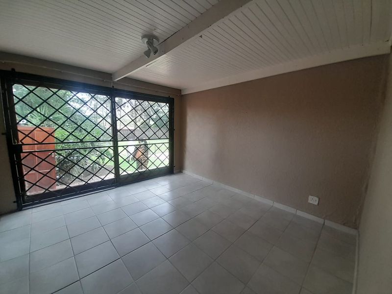 A covered patio area featuring tiled flooring, a secure sliding glass door, and a white tongue and groove ceiling.