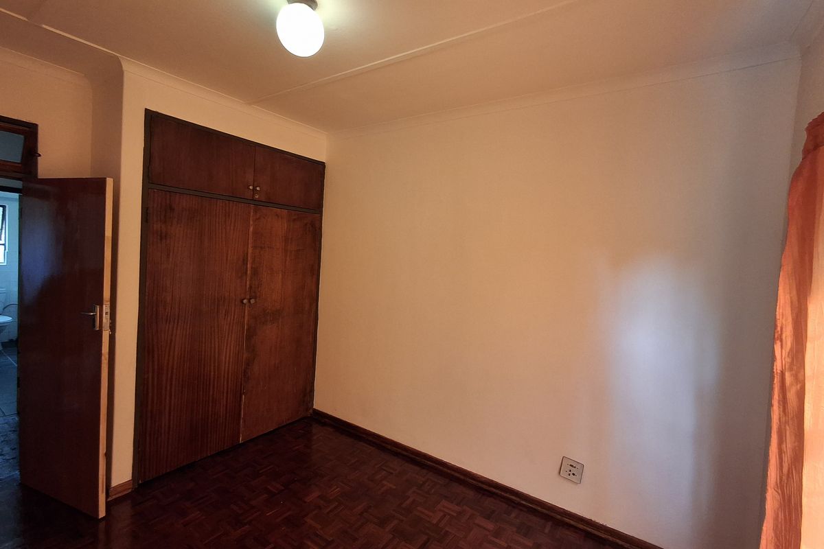 A vacant bedroom featuring classic parquet flooring and built-in wooden cupboards, offering a neutral space ready for personalization.