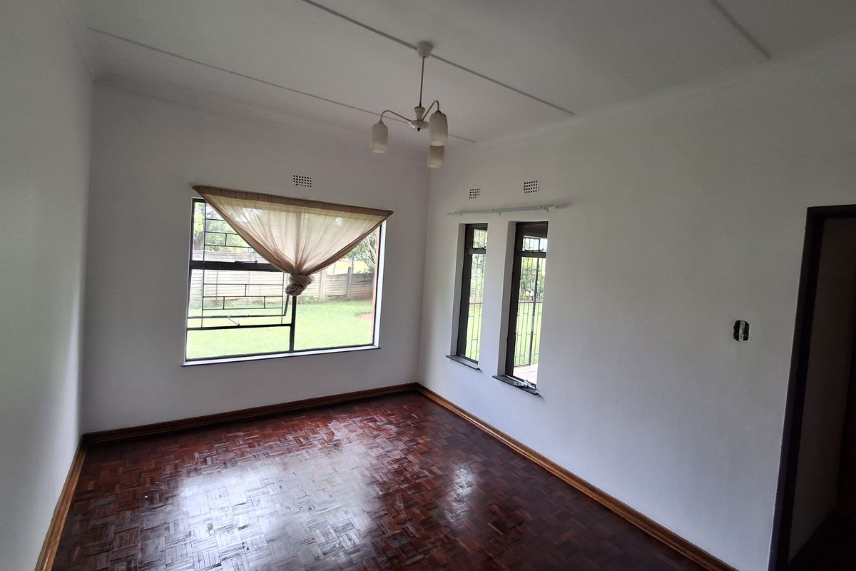 A bright, empty living room featuring polished parquet flooring, timber skirting boards, and steel-framed windows with security bars.