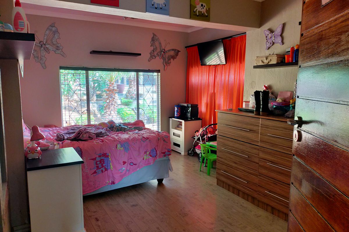 A bedroom featuring laminate flooring, security bars on the window, and a solid timber door.