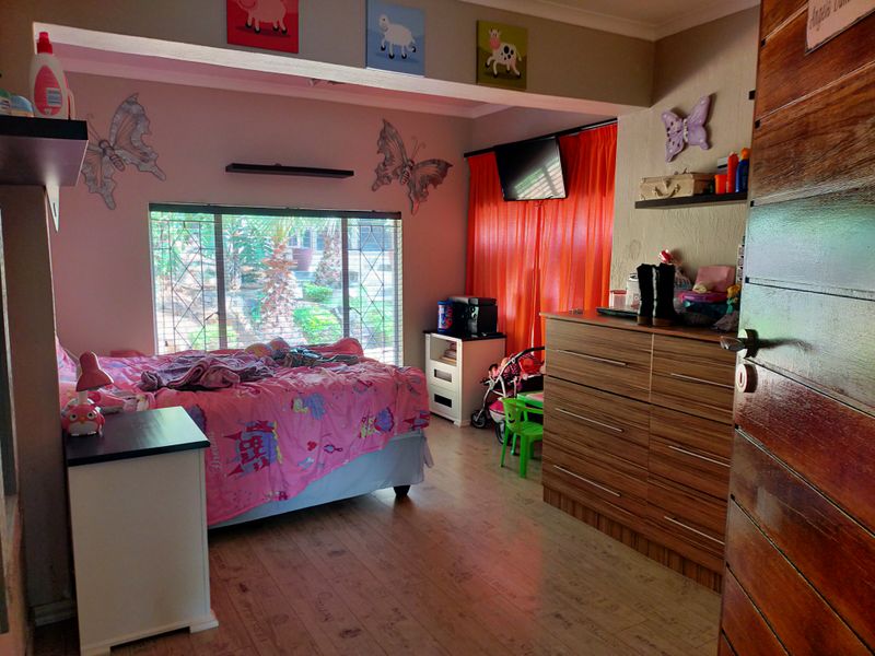 A bedroom featuring laminate flooring, security bars on the window, and a solid timber door.