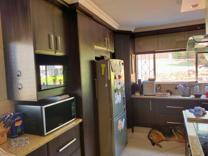 A functional kitchen featuring dark wood cabinetry, granite countertops, built-in microwave, and an extractor fan, with tiled flooring and natural light.