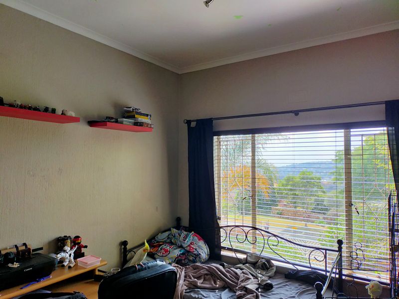 A bedroom featuring a large window with security bars, built-in wall shelving, and neutral wall finishes.