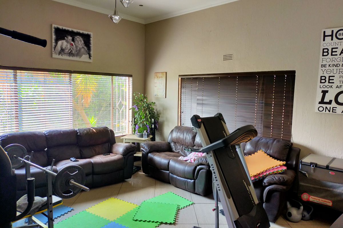 A spacious living area featuring tiled flooring and large windows with venetian blinds, currently utilized as a multi-purpose room.