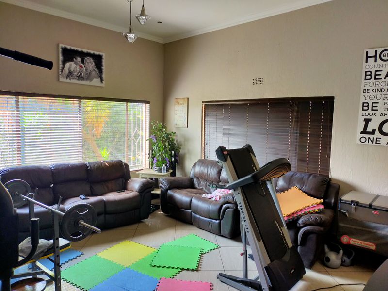 A spacious living area featuring tiled flooring and large windows with venetian blinds, currently utilized as a multi-purpose room.