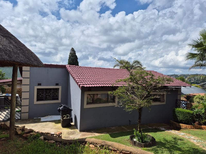 Rear view of the property featuring a tiled roof, security bars on windows, a thatched lapa, and a landscaped garden area.