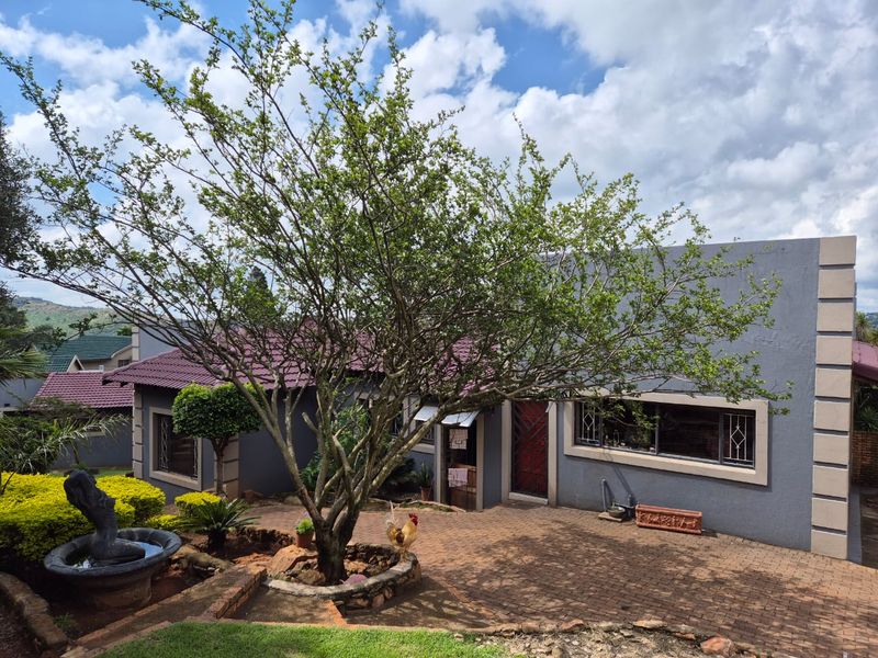 Front exterior view of a house featuring a paved driveway, mature tree, stone-edged garden bed, and security features on windows and doors.