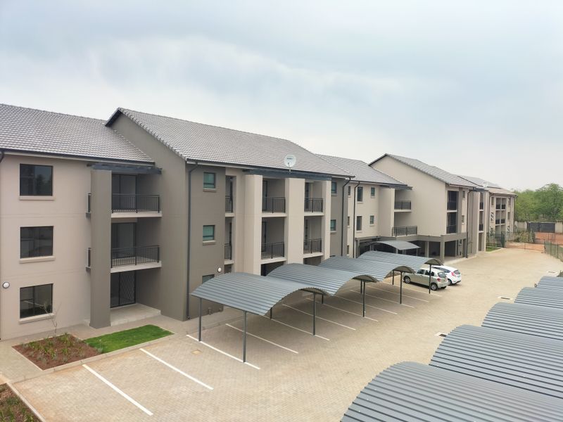An elevated view of a modern apartment complex featuring multi-level balconies, covered parking bays, and a paved driveway area.