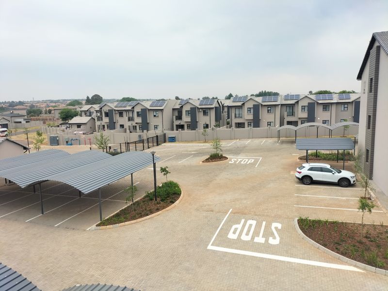 An aerial view of a modern apartment complex featuring paved parking areas, covered carports, and residential units equipped with rooftop solar panels.