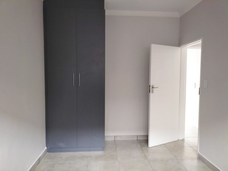 A clean, empty bedroom featuring neutral wall paint, modern grey built-in wardrobes, and light-colored floor tiles.