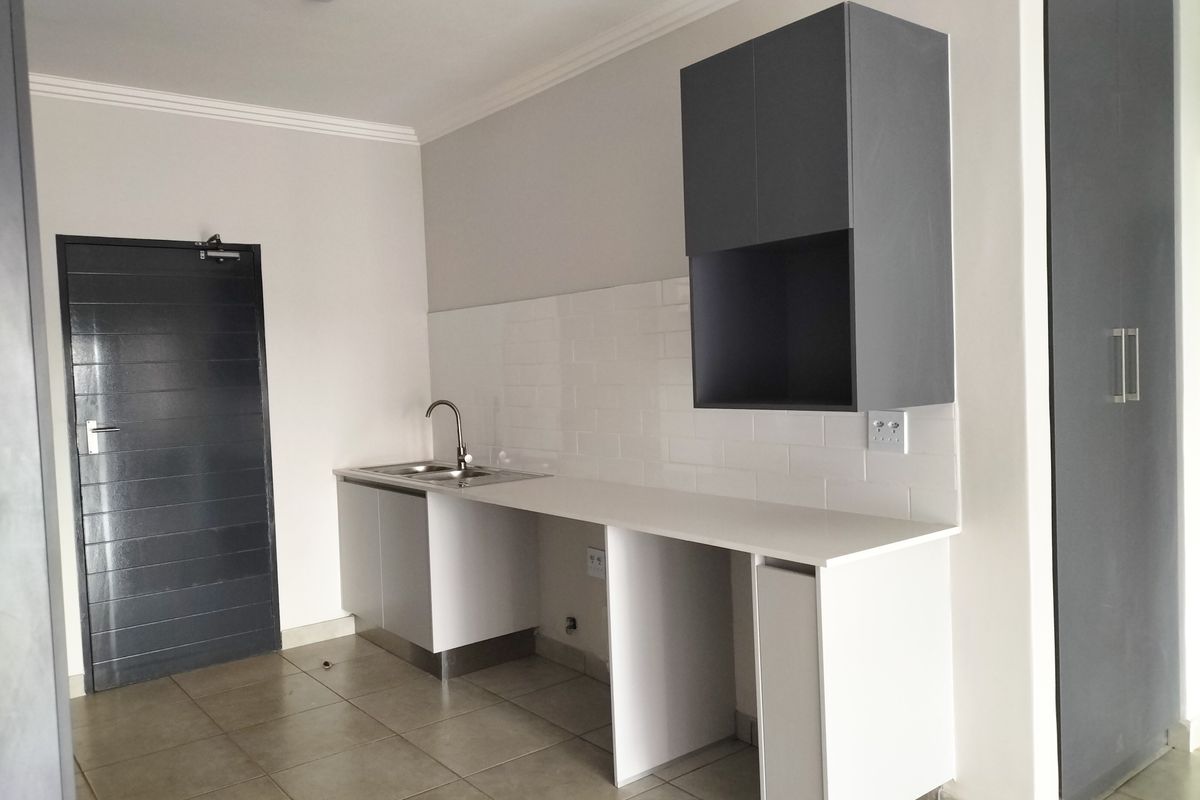 A clean, modern kitchen area featuring white cabinetry, a subway tile backsplash, quartz countertops, and a stainless steel sink.
