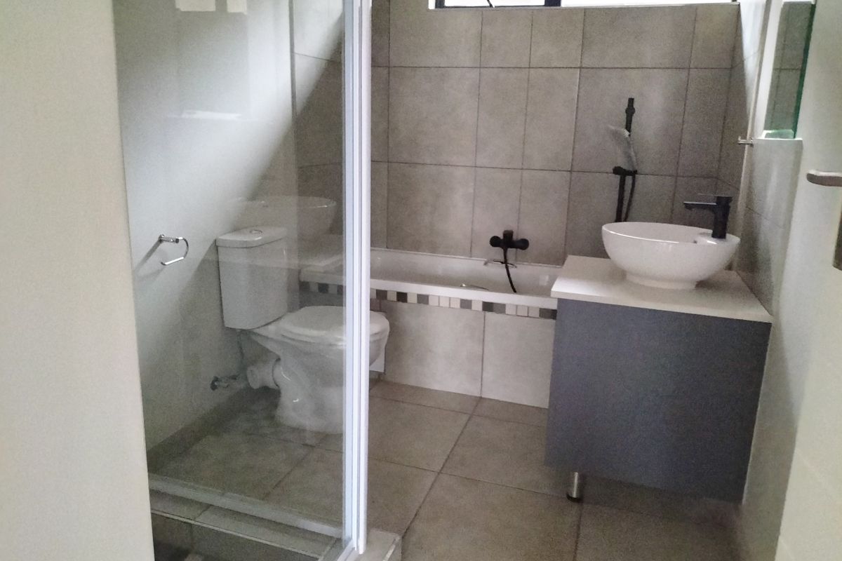 A modern bathroom featuring a glass-enclosed shower, a bathtub, a vessel sink on a vanity cabinet, and neutral wall and floor tiling.