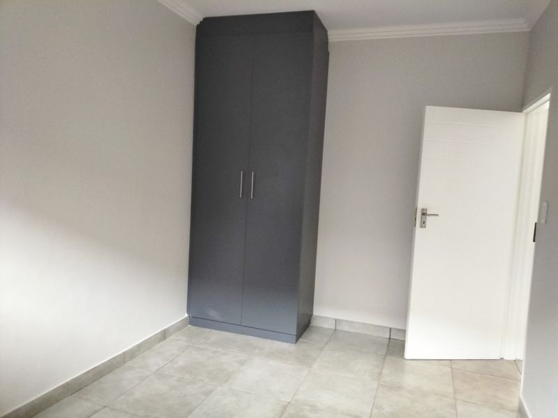 A clean, empty bedroom featuring neutral tiled flooring, a modern dark grey built-in cupboard, and crisp white walls with crown molding.