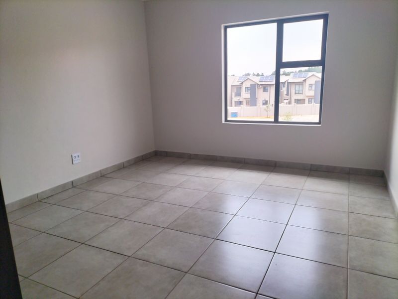 A clean, empty bedroom featuring neutral tiled flooring, modern aluminium window frames, and smooth wall finishes, ready for personalization.