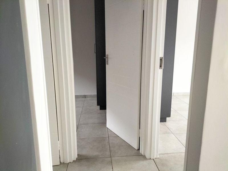 A clean, modern hallway featuring neutral tiled flooring and white internal doors with contrasting dark wall accents.