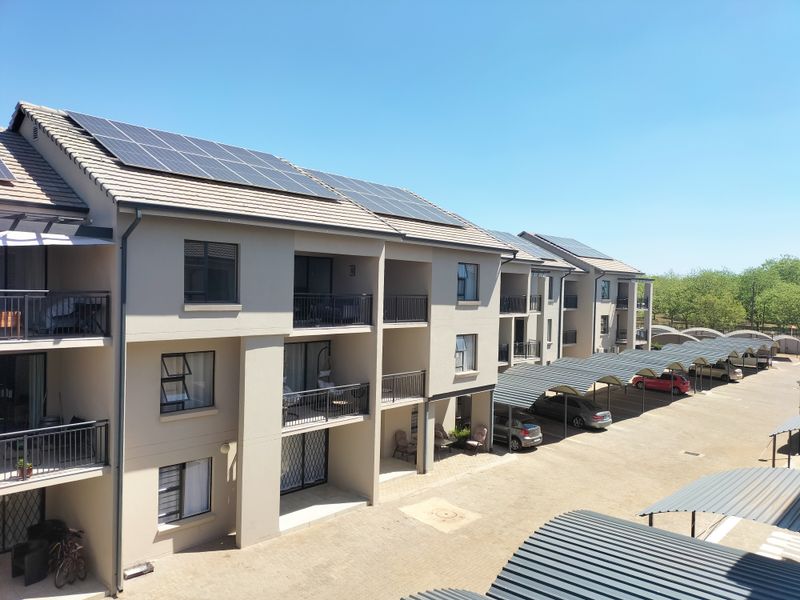 Exterior view of a modern apartment complex featuring solar panels on the roof, private balconies, and covered carport parking spaces.