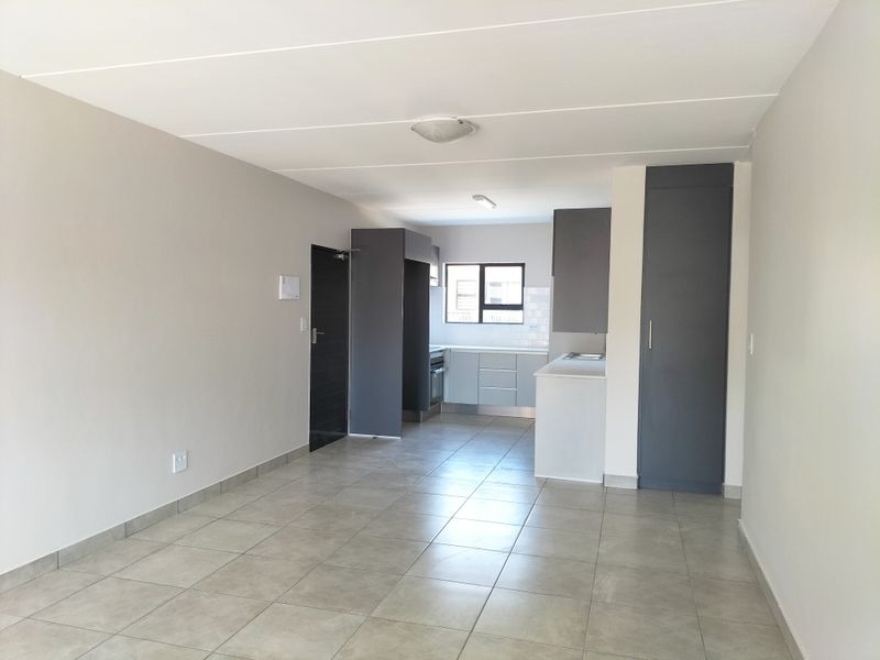 An open-plan living and kitchen area featuring modern grey cabinetry, built-in appliances, and neutral tiled flooring throughout.