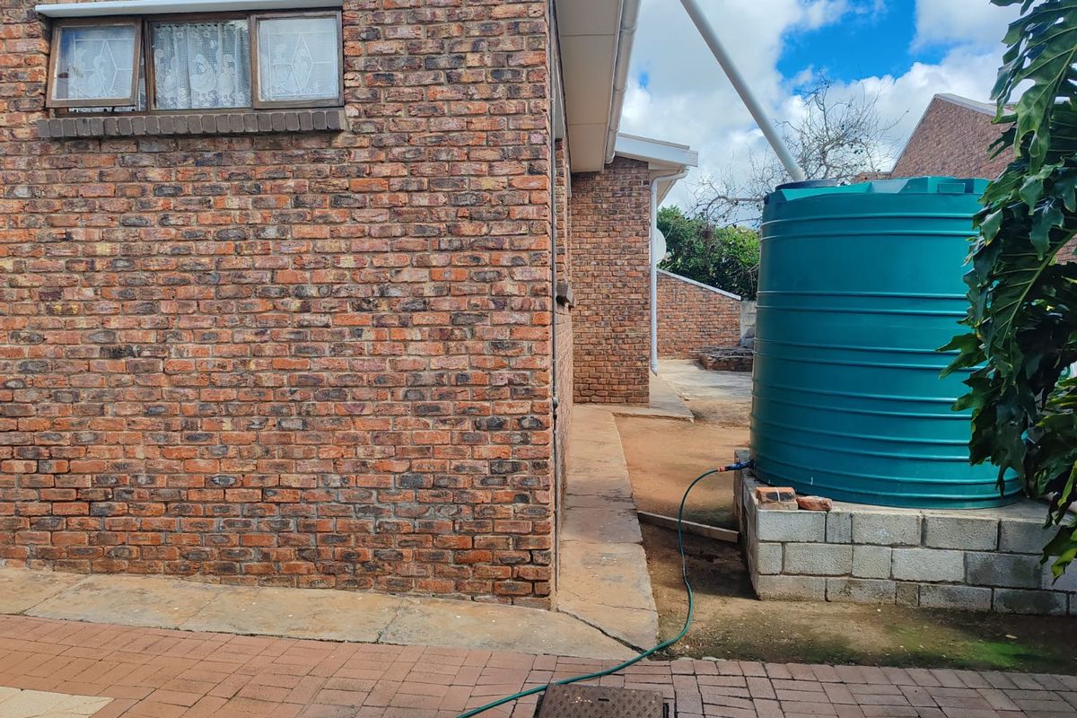 Rear exterior view of the property featuring face brick walls, a paved walkway, and a large water storage tank on a concrete block base.